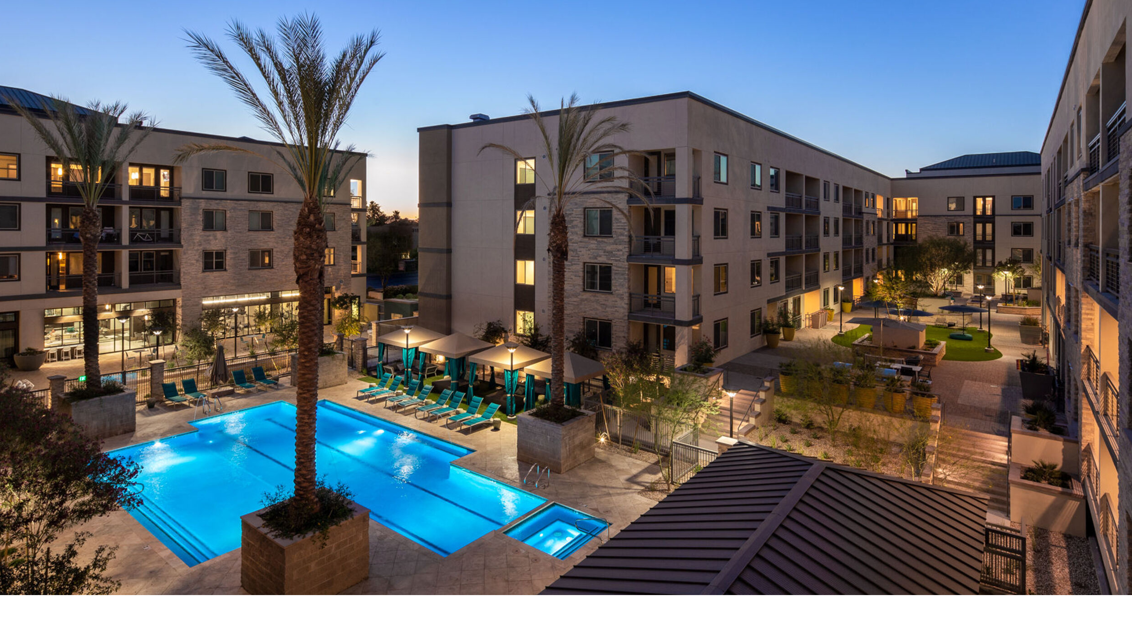 Peak 16 apartment courtyard at twilight with swimming pool, landscaped deck and surrounding multifamily buildings.